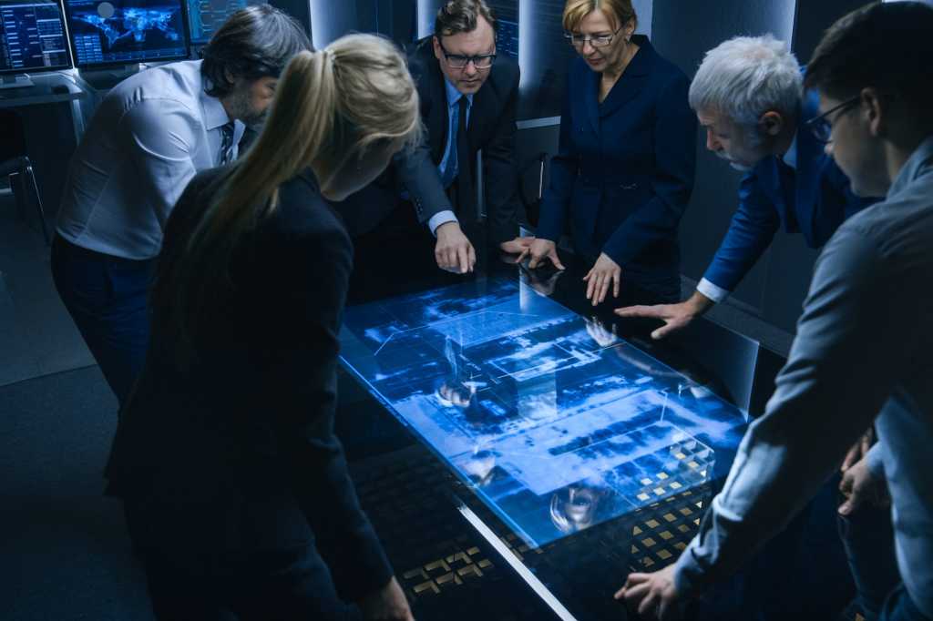 A team of government intelligence officers / FBI agents review data via digital touch screen.