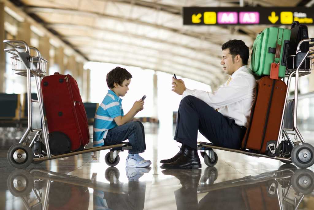 Man and boy in airport using wireless or cellular phones