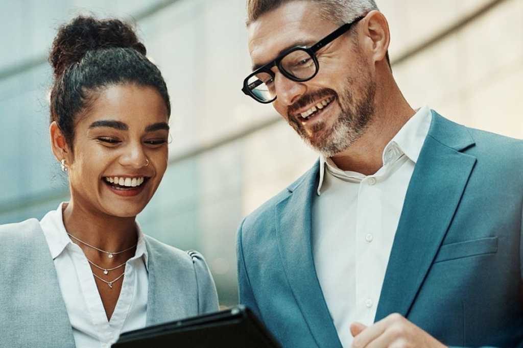 Man and Woman in office collaborating on a tablet smiling